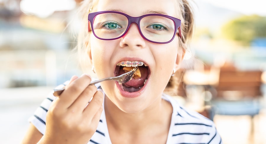 Young girl in glasses and wearing braces eating soft food